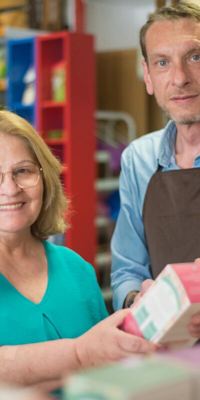 A senior woman and shopkeeper smiling during a grocery interaction in Portugal.